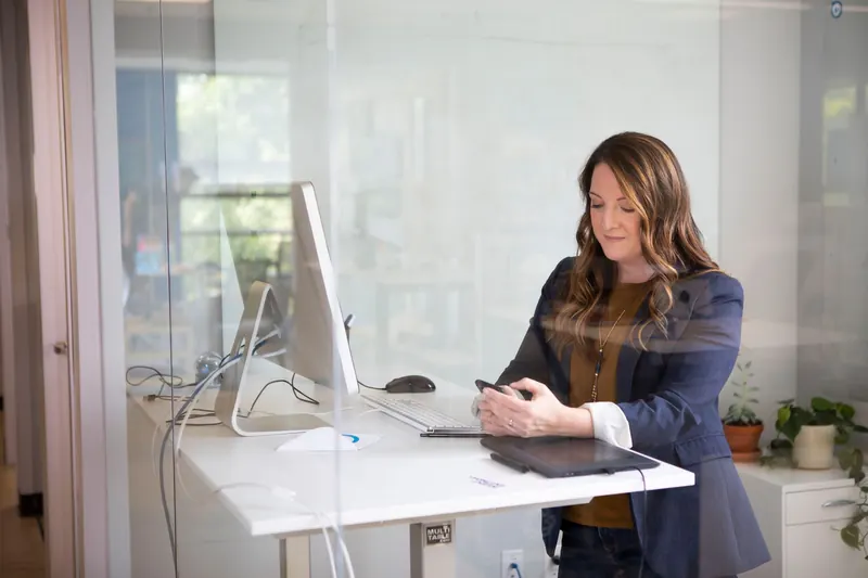 Businesswoman in a blazer using her smartphone at a standing desk in a modern office