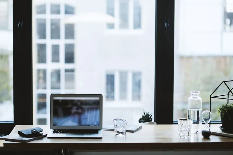 Sleek office desk setup featuring a laptop, glass of water, and open window view